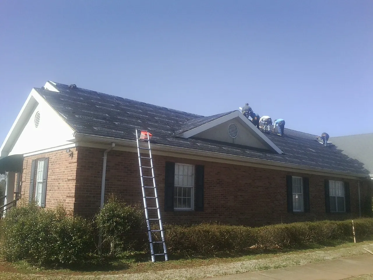 Crew tearing shingles off a brick ranch roof with a ladder set — Metal Roof Repair work by our crew in San Gregorio