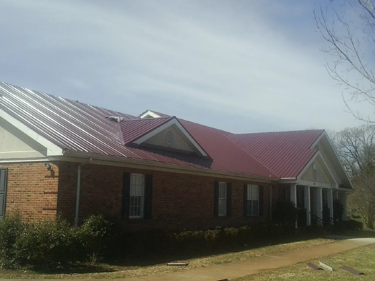 Red metal roof with gabled entries on a long brick building, from a Hail Damage Roof Repair job in San Gregorio