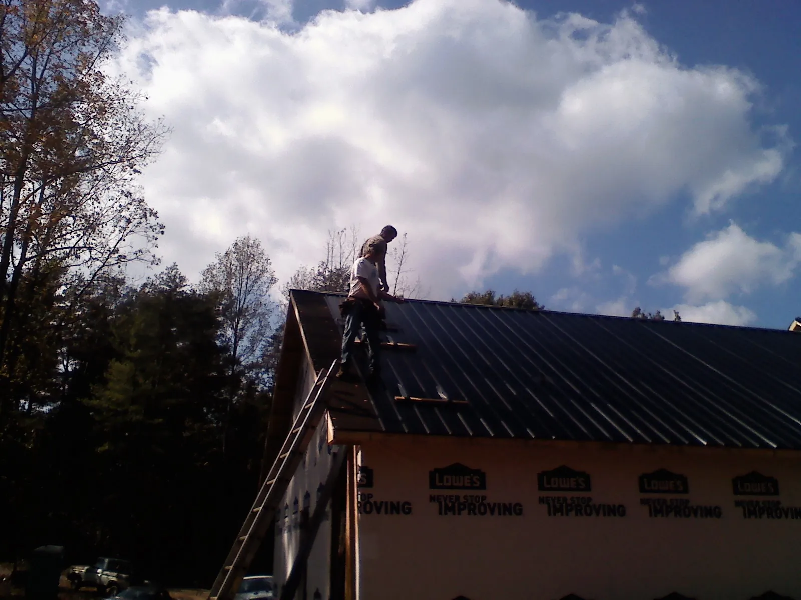 Roofer fastening dark metal panels high against a cloudy sky, from a Roof Inspection job in San Gregorio